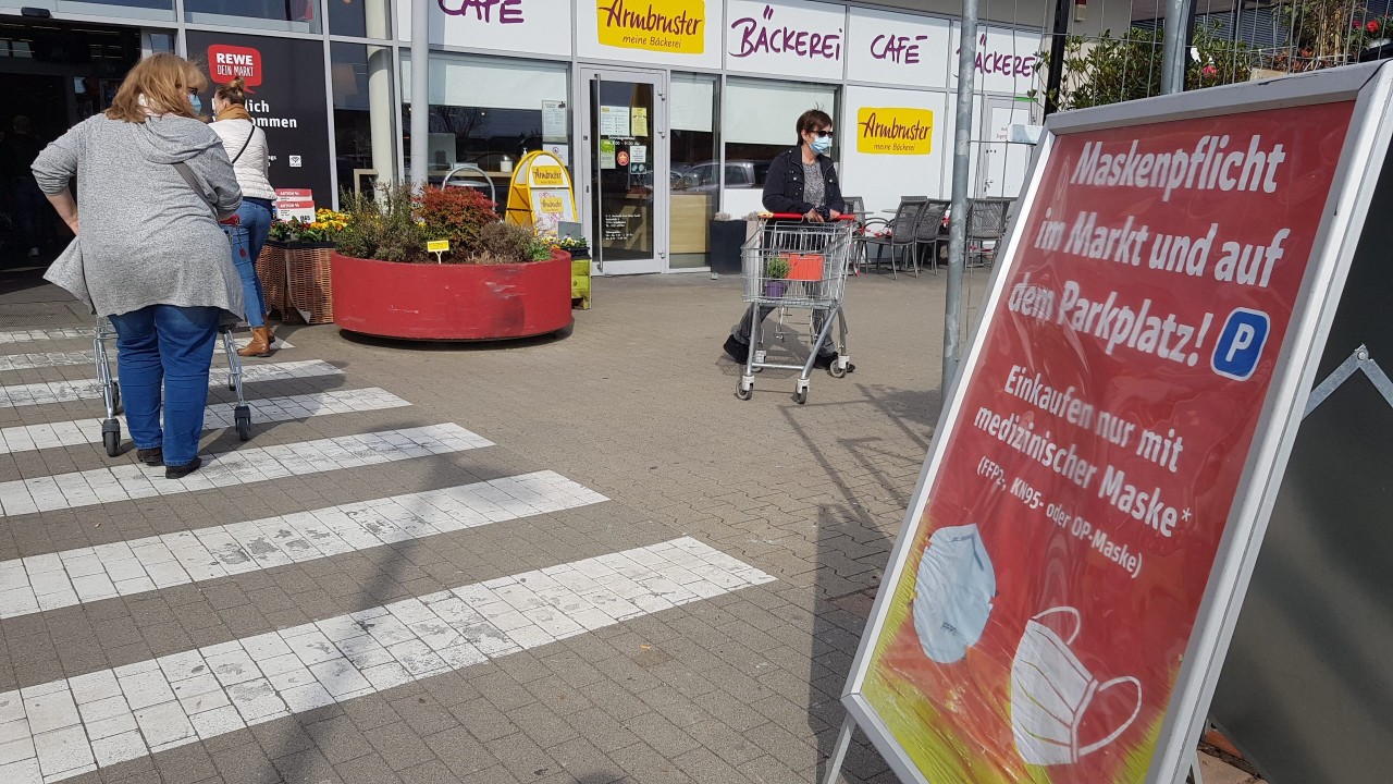 Hinweis auf die Maskenpflicht auf einem Rewe-Parkplatz.