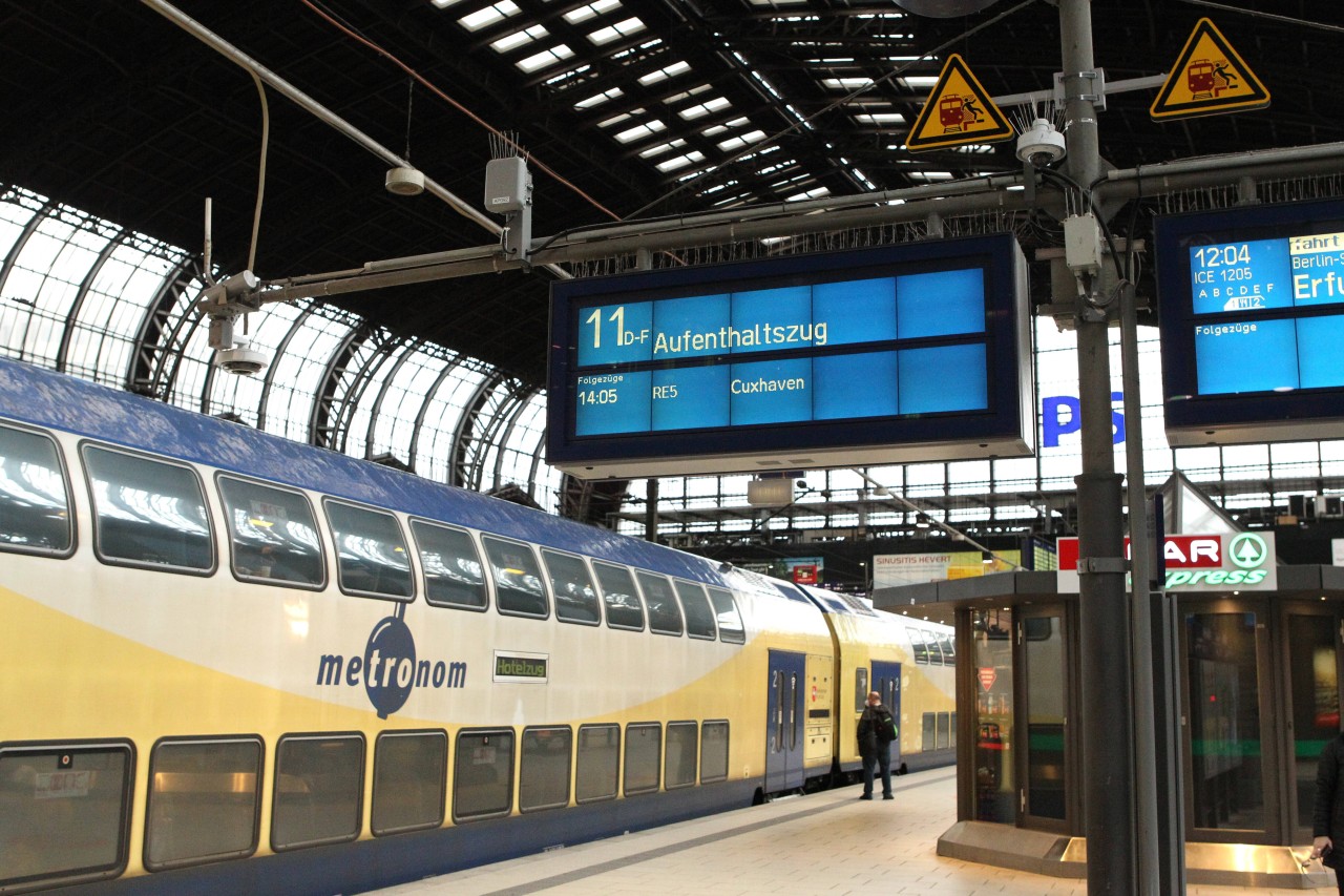 Zugzielanzeiger im Hauptbahnhof Hamburg. Auf dem Gleis steht ein Metronom, der den wartenden Fahrgästen als Aufenthaltszug dient.