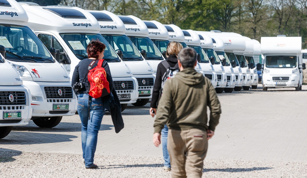 Interessenten, die ein Wohnmobil mieten oder kaufen wollen, schlendern über einen Parkplatz.